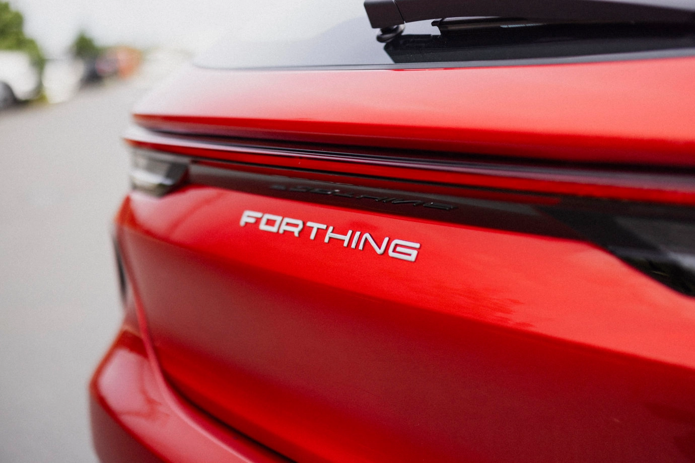 Close-up of the rear end of a red car, focusing on the badge that reads 'FORTHING' on the trunk panel.