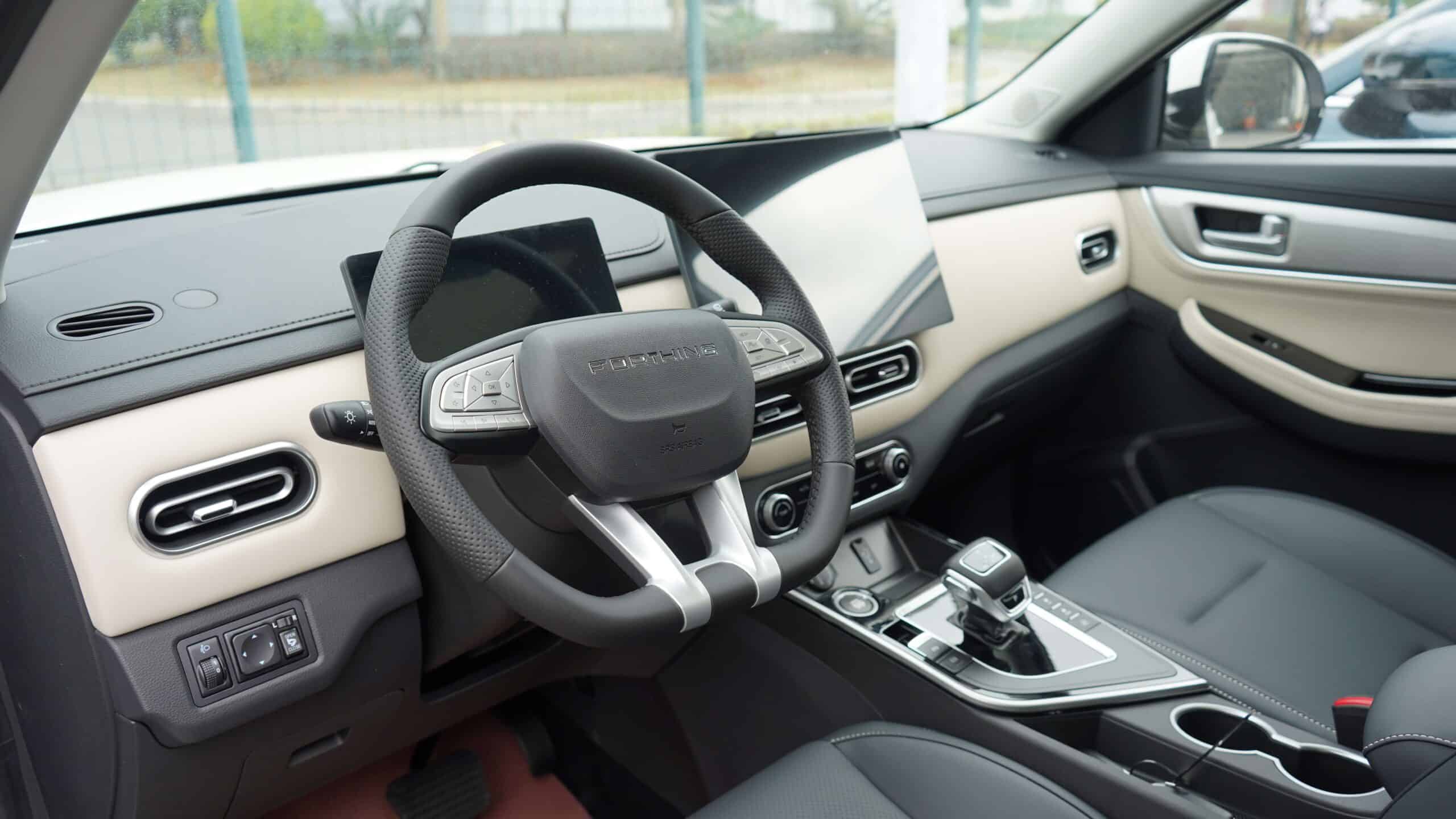 Inside view of a modern car's beige and black dashboard with a central steering wheel and digital display panel behind it.
