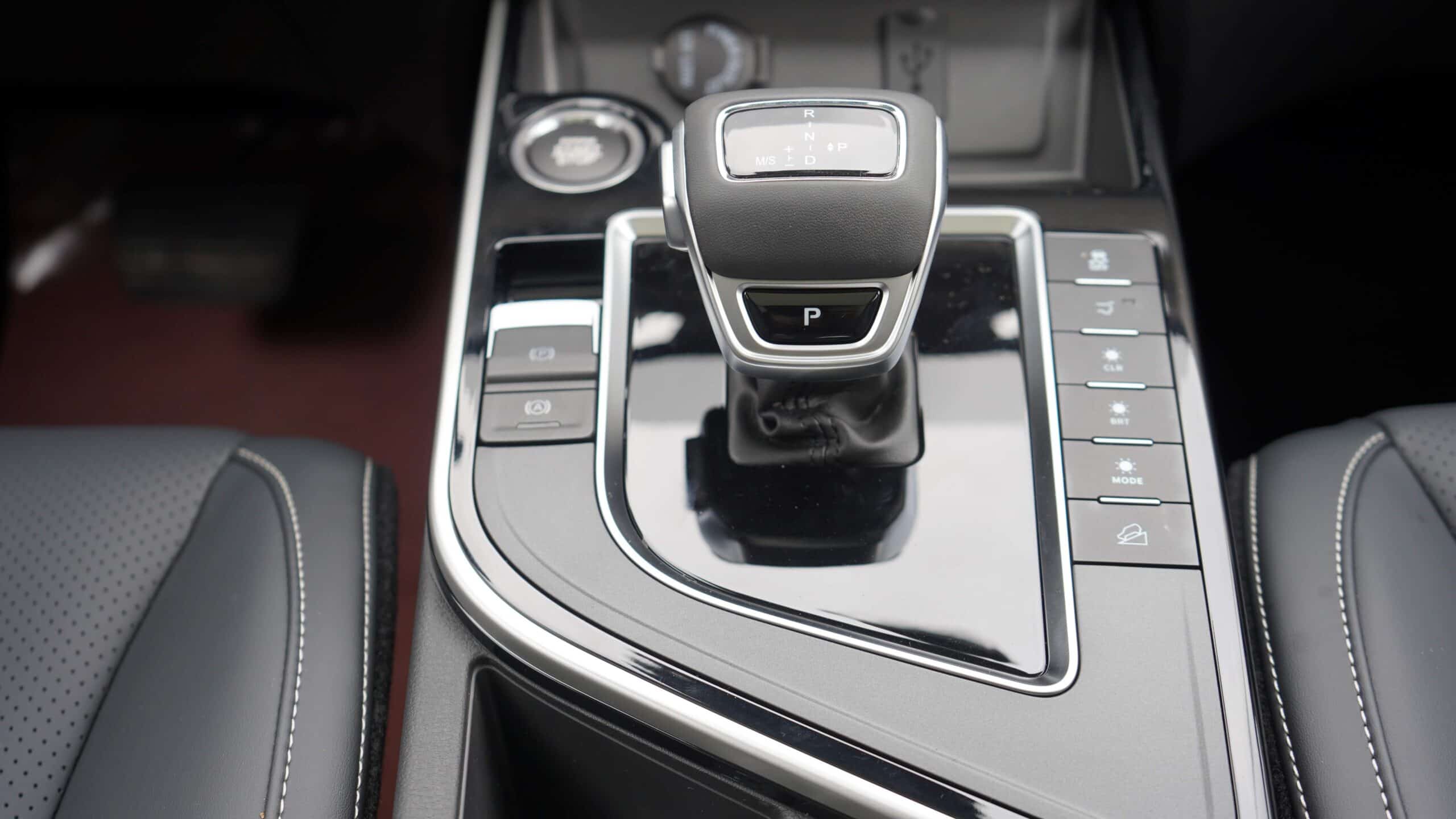 Close-up of a car's gear shift lever on the center console with surrounding glossy panels and control buttons