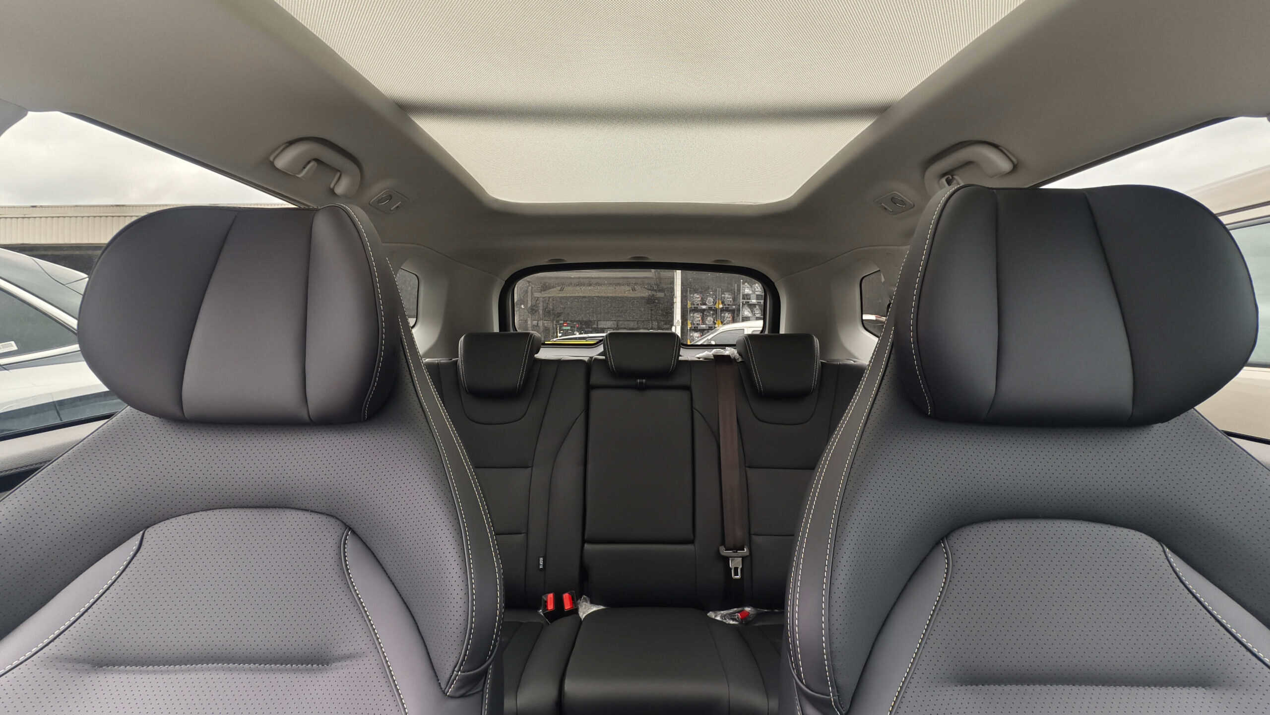 Rear passenger seats in a modern car with gray perforated upholstery and a large sunroof overhead.