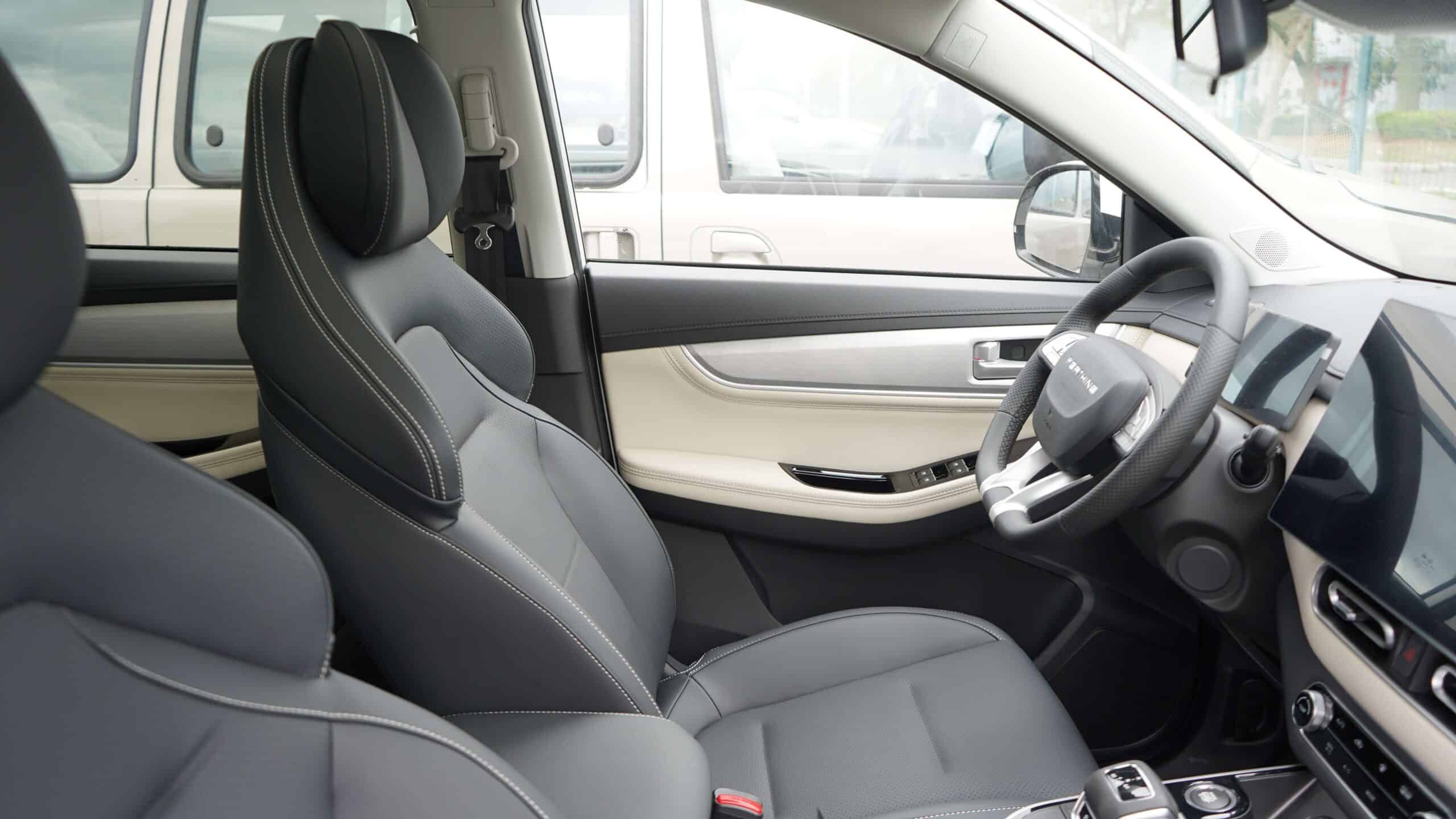 Interior view of a modern car cabin: front driver and passenger seats with black leather and white stitching, beige door panel, and steering wheel visible.
