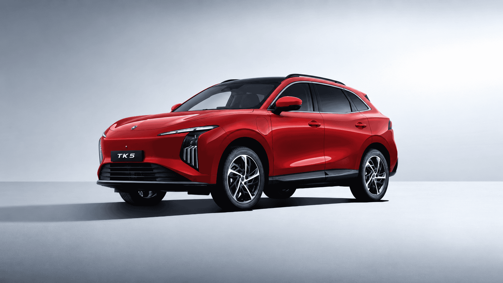 Red compact SUV photographed from a front-right angle, showing its bold grille and slim headlights in a studio setting.
