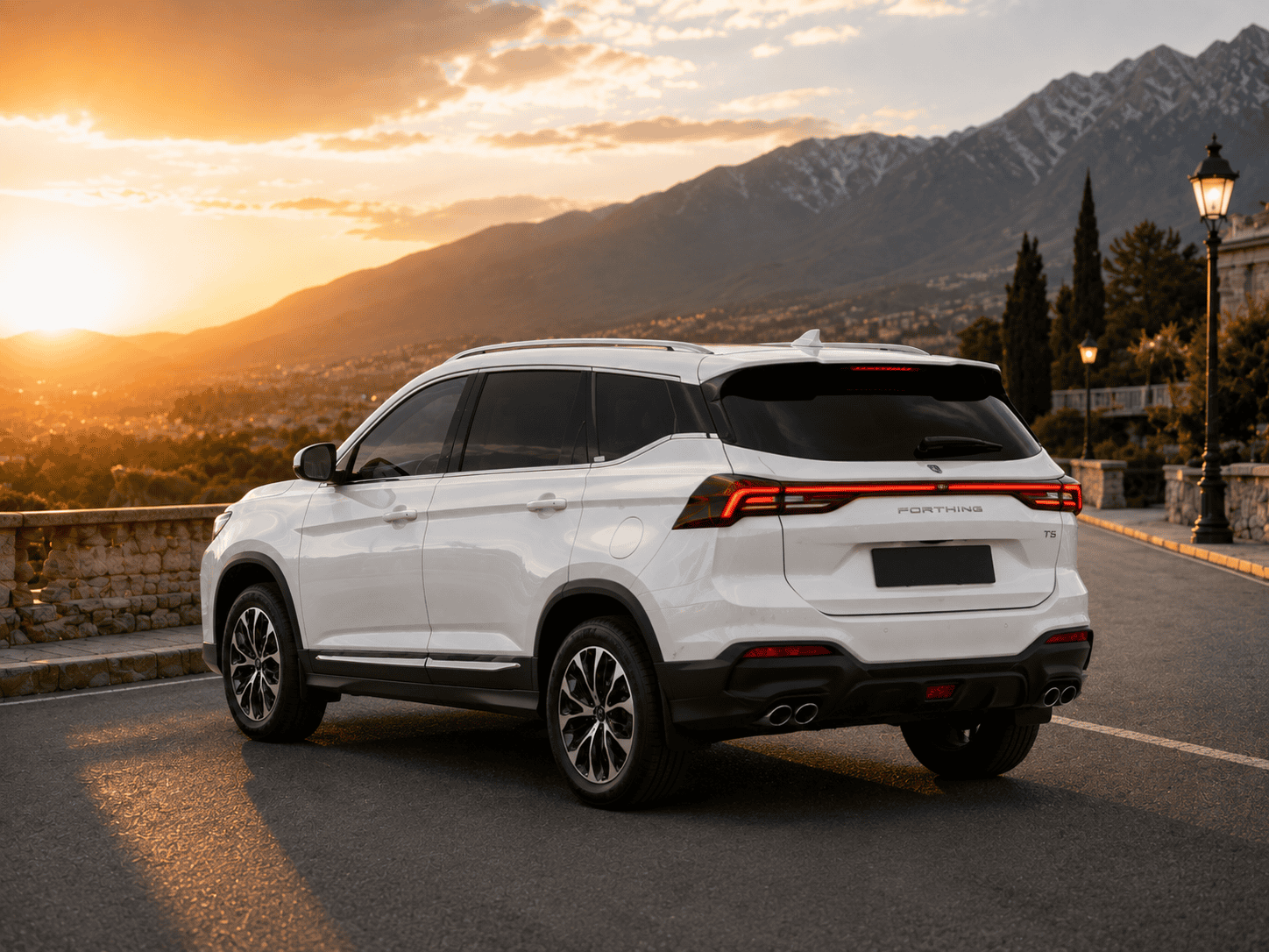 White SUV parked on a mountain road at sunset, with a mountain range and town in the distance.