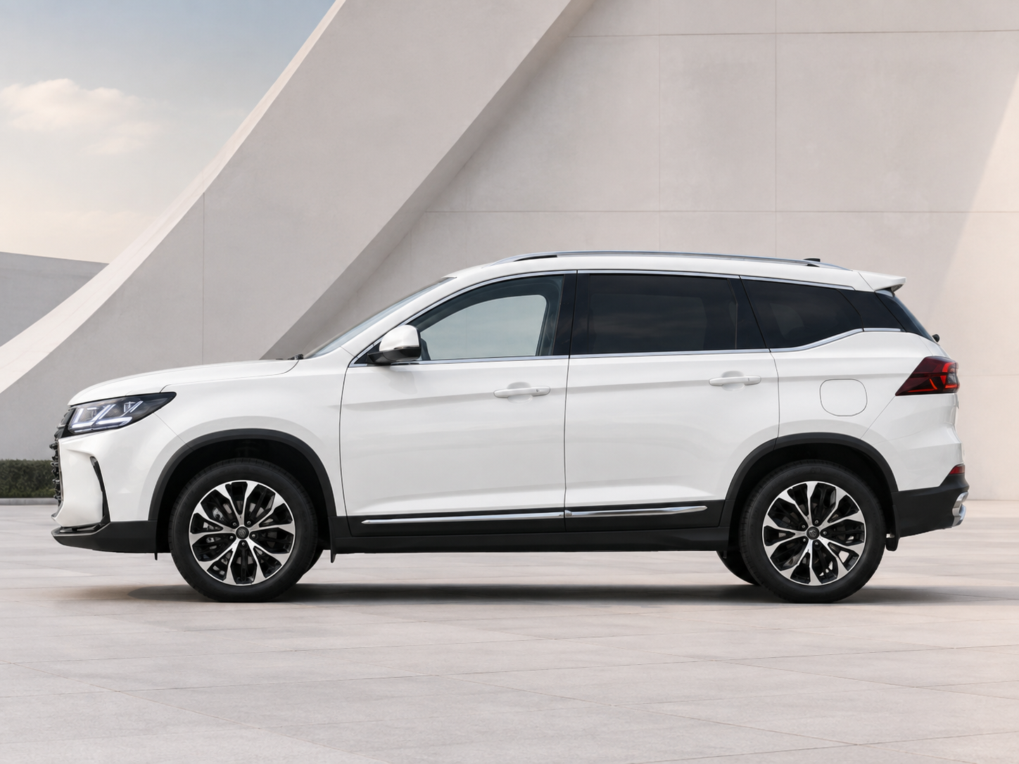 Side view of a white SUV with black trim and alloy wheels, parked on a light-gray plaza with a modern architectural backdrop