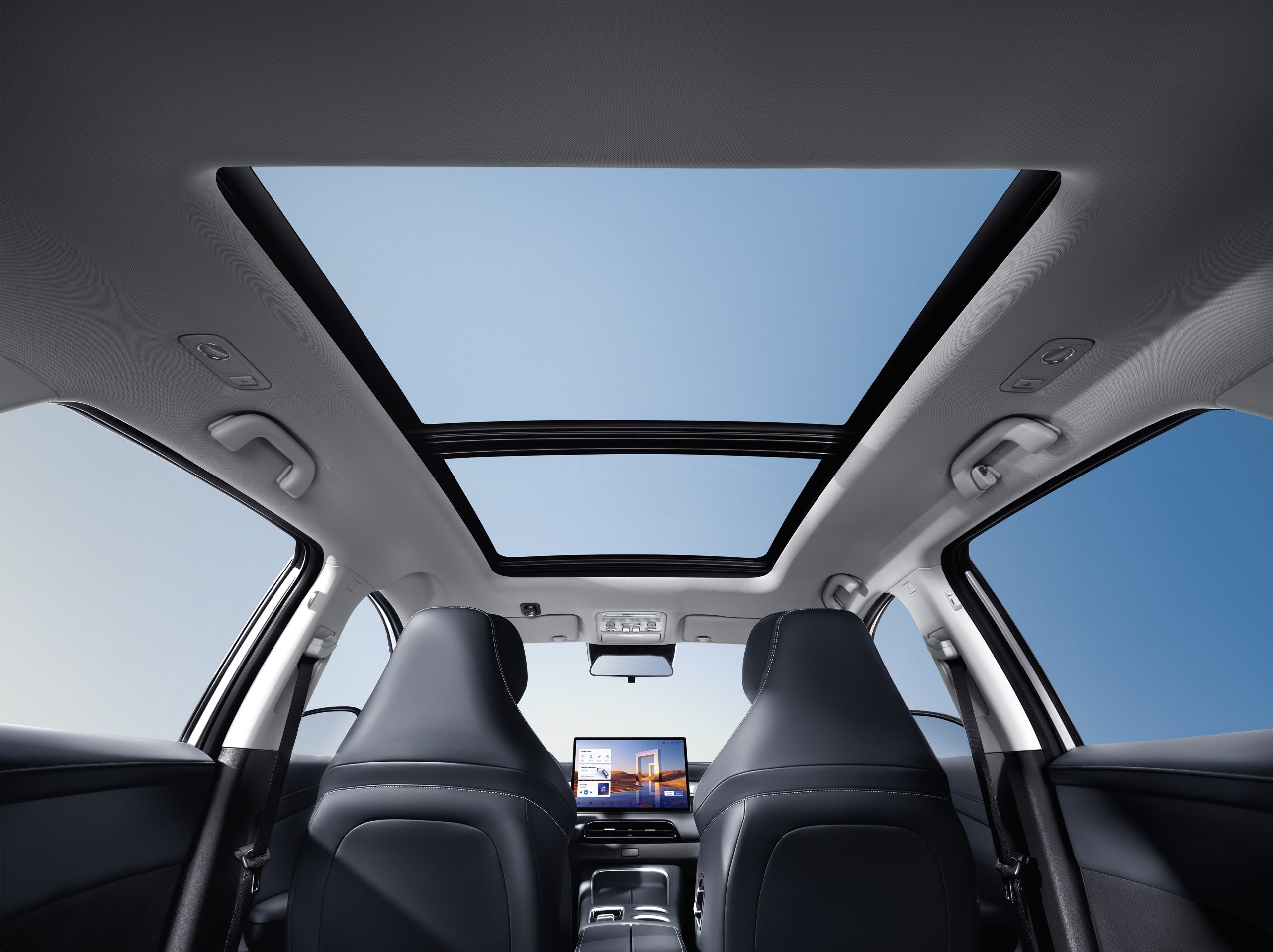 Interior of a car cabin with a large panoramic sunroof showing a clear blue sky