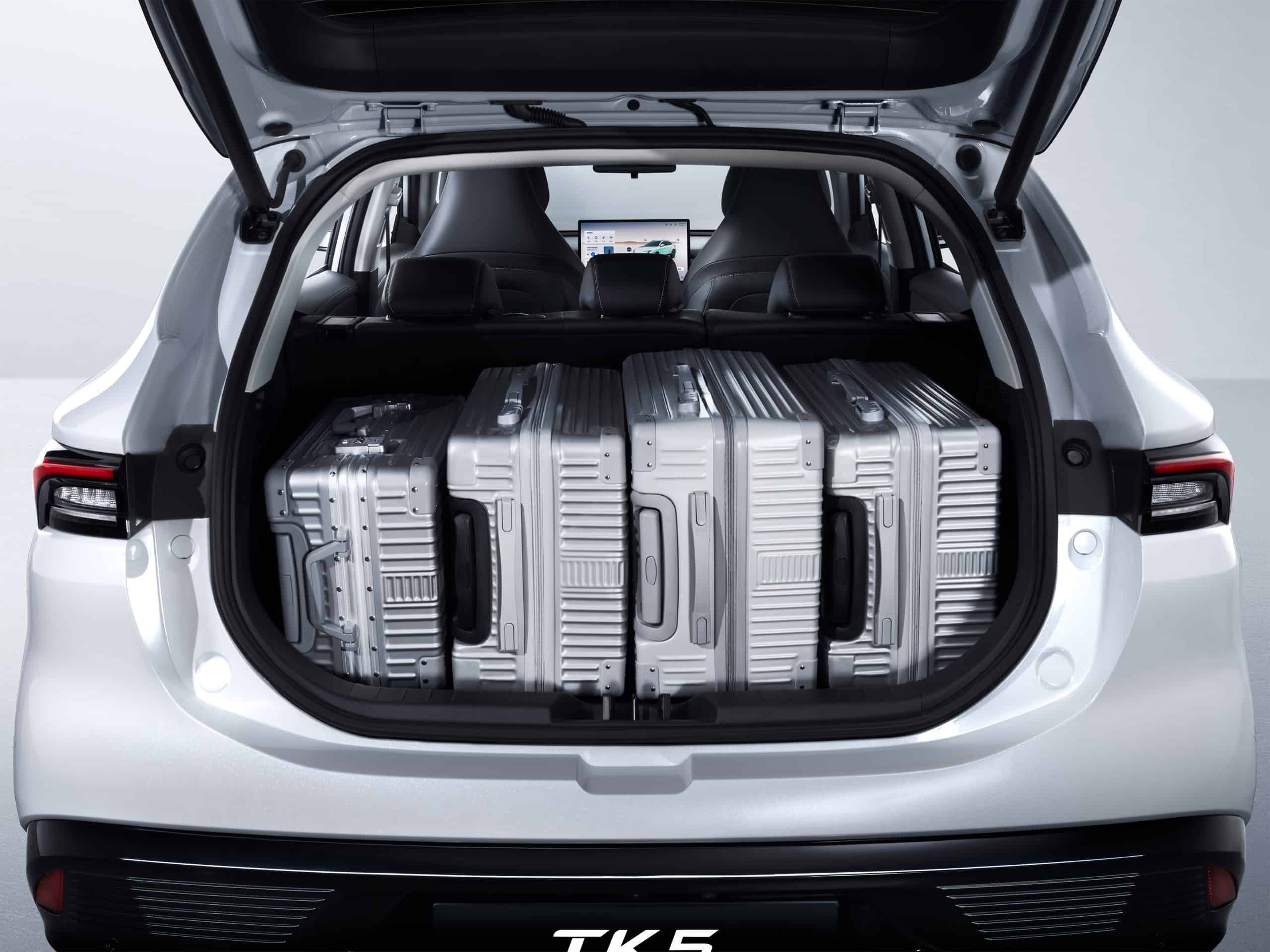 Open SUV trunk filled with four silver hard-shell suitcases in the cargo area, white exterior, rear seats upright, car model badge visible below.